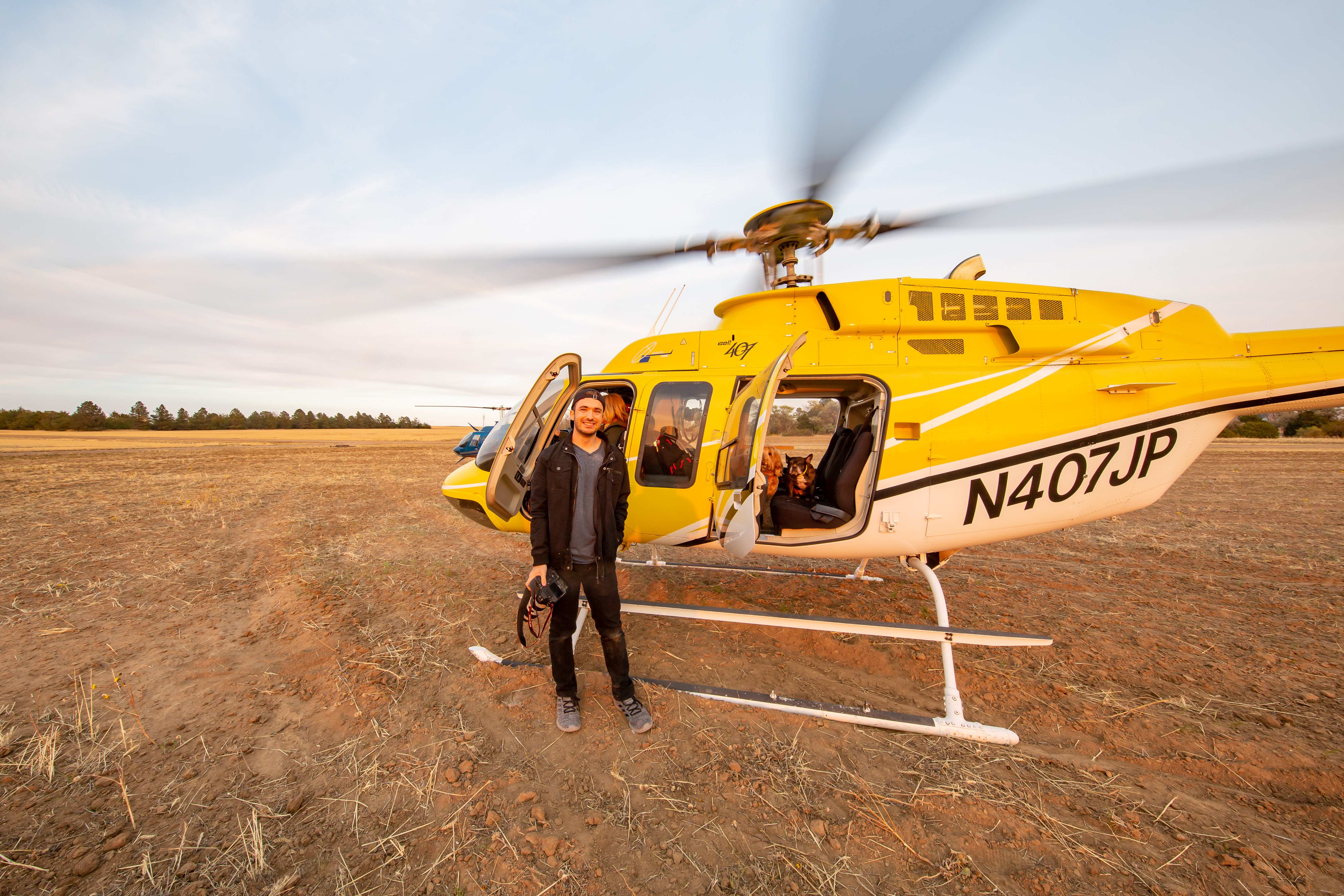 Billy Hardiman standing by yellow Bell 407 helicopter with rotors spinning