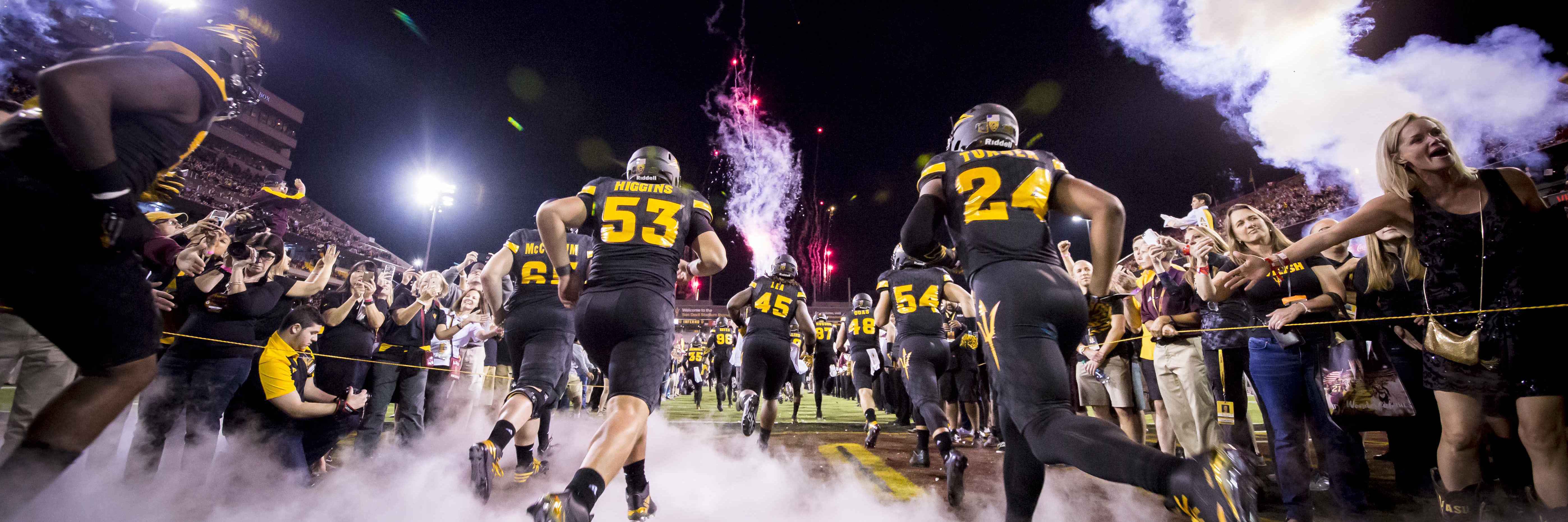 Arizona State football team entering field with smoke and fireworks, fans cheering in Tempe, AZ