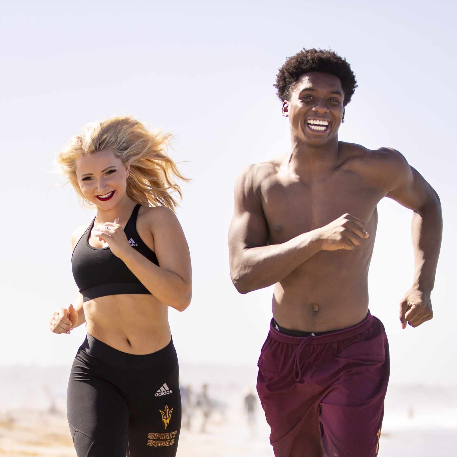 Young man and woman running barefoot on beach with joyful expressions