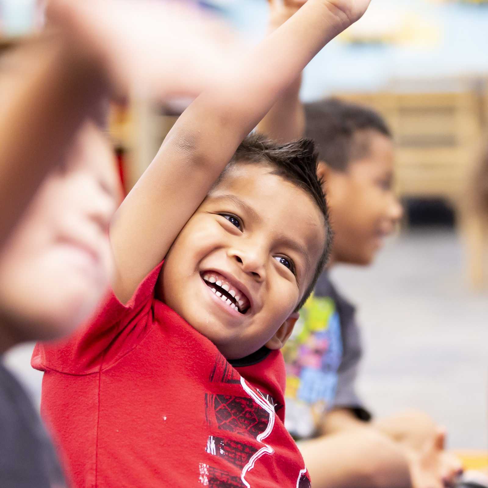 Young student raising hand in classroom with excited expression