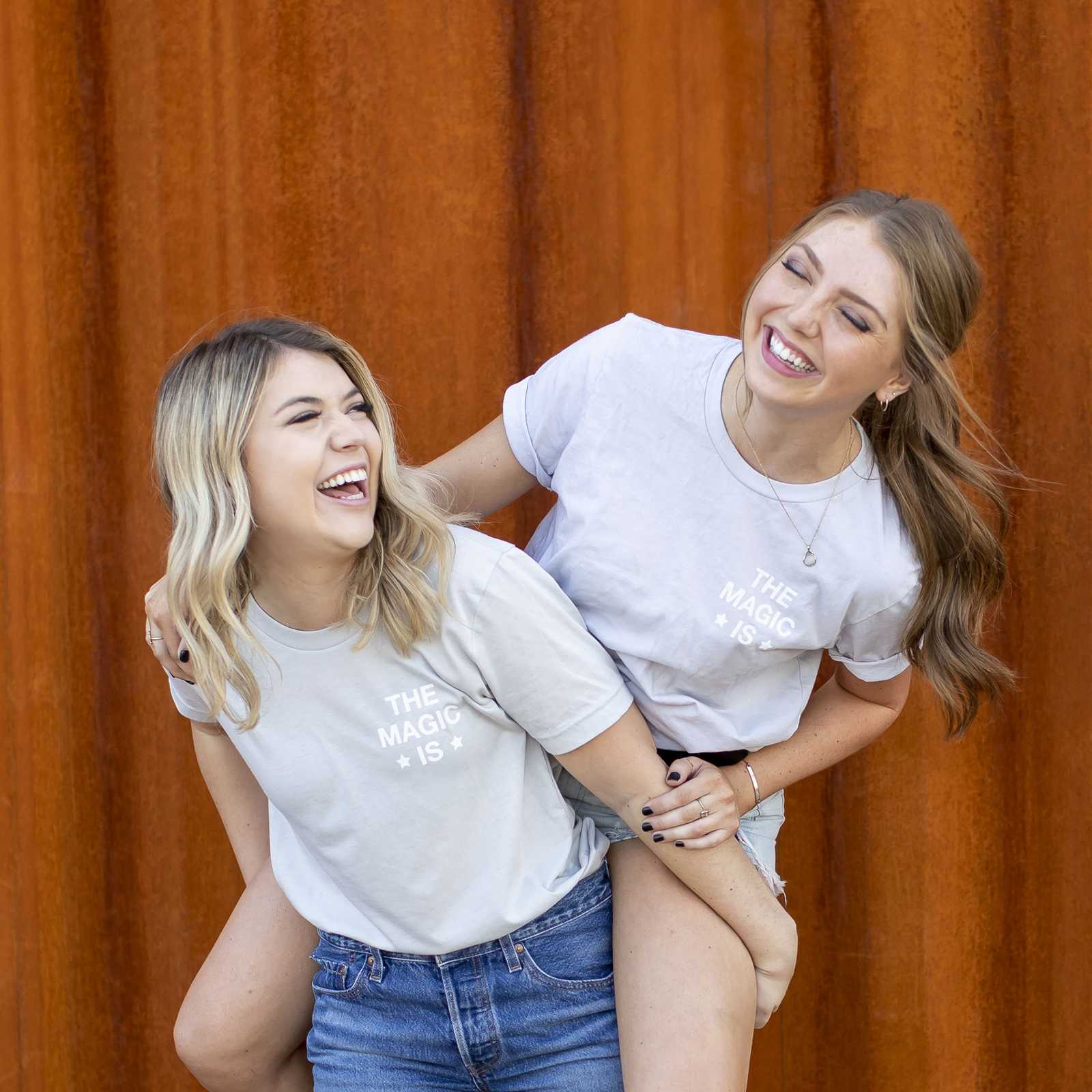 Two young women laughing in front of a rust-colored wall in Downtown Phoenix, Arizona