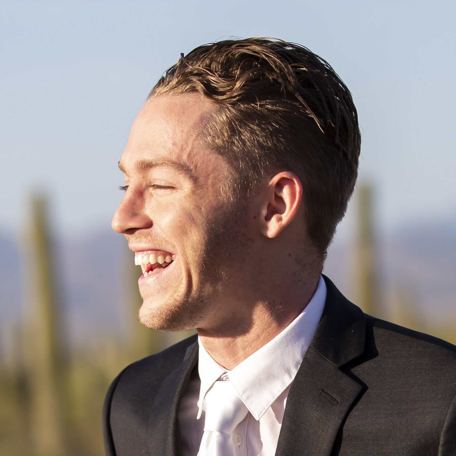 Young man in a suit laughing with desert and cacti in background