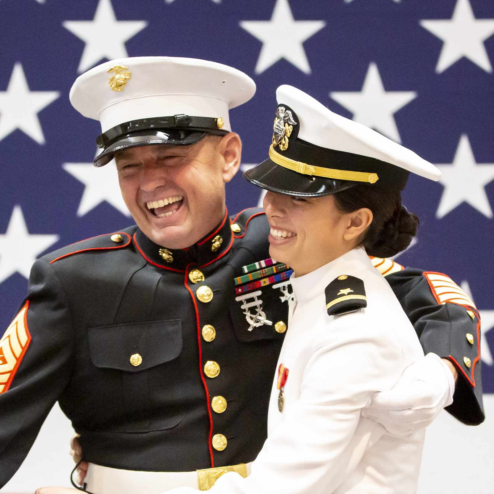 Two military personnel embracing and laughing during a Navy ROTC commissioning ceremony at Arizona State University