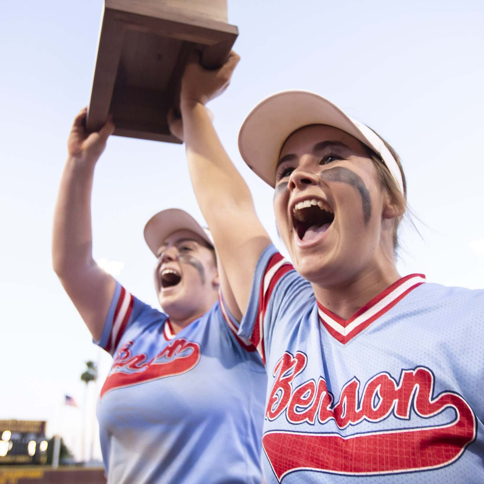 Two high school softball players lifting a trophy and cheering