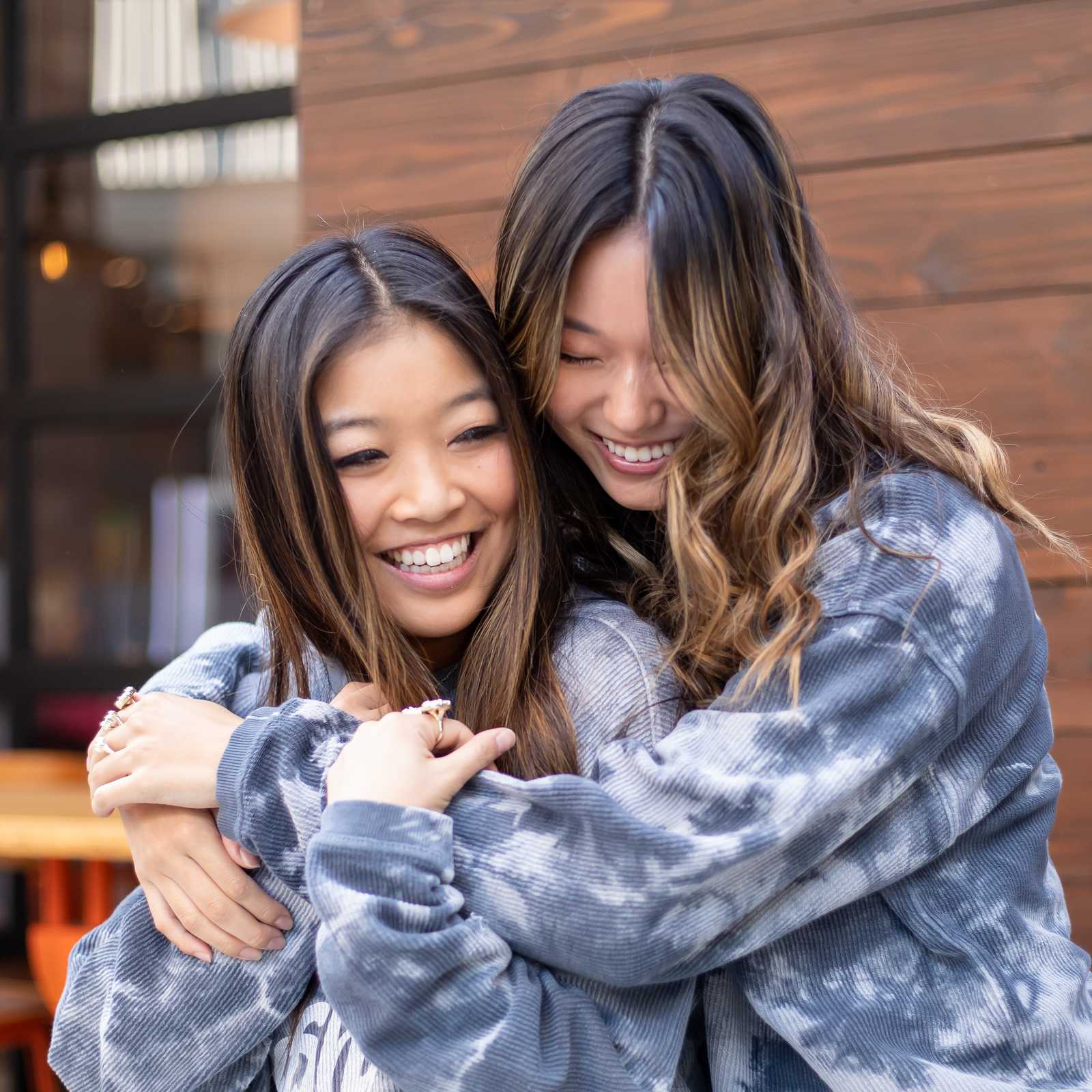 Two young sorority friends hugging and smiling outdoors at a mall in Los Angeles, California