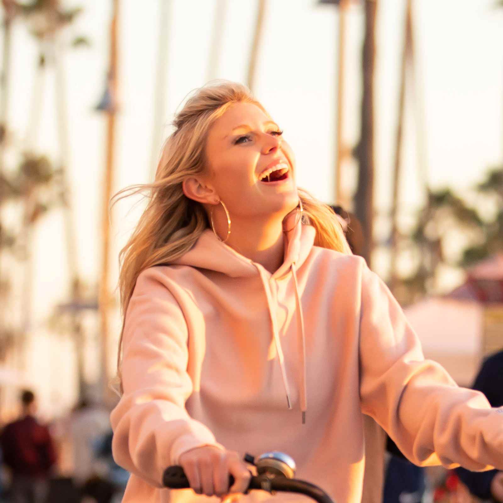 Young woman laughing while riding her bike on Venice Beach Boardwalk in Los Angeles, California