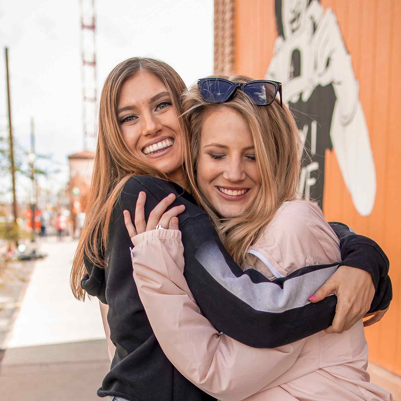 Two young women smiling and hugging on a city street in Tucson, Arizona